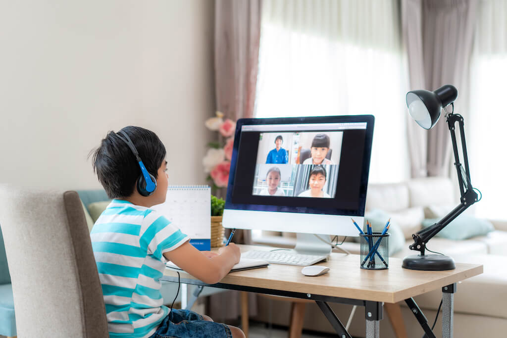 Seorang anak laki-laki yang duduk di depan iMac yang berpartisipasi dalam kelas langsung