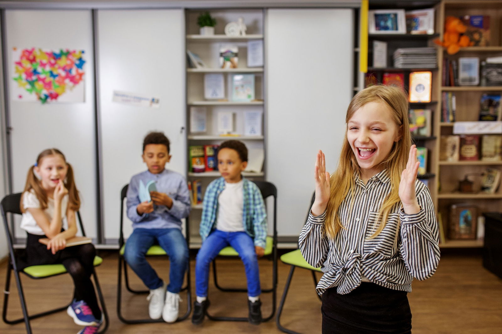 schoolgirl participating in phonics activities in class doing charades in front of classmates and teachers